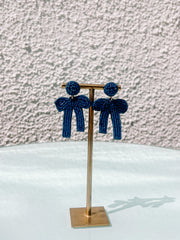 Pair of blue beaded earrings on a gold stand against a textured wall.