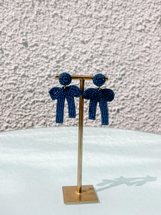 Pair of blue beaded earrings on a gold stand against a textured wall.