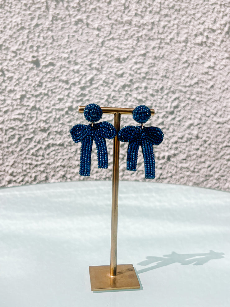Pair of blue beaded earrings on a gold stand against a textured wall.